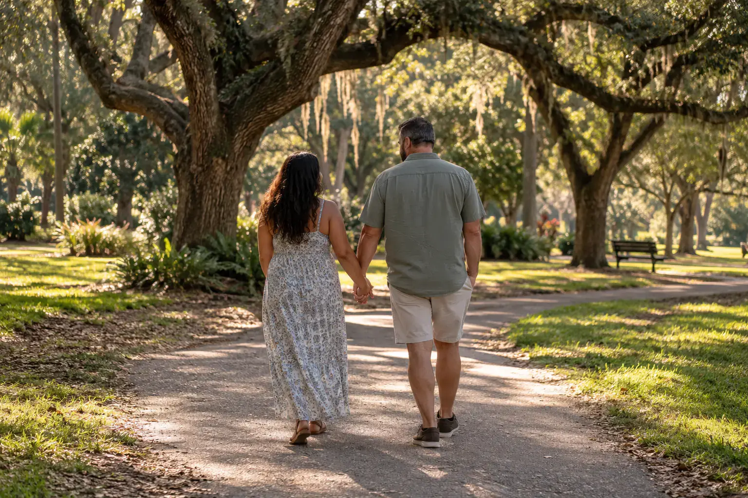 A couple walking hand in hand along a shaded park path.