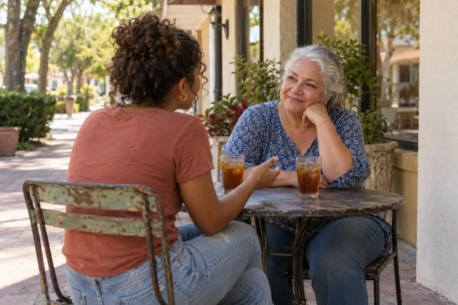 A young woman talking with an older woman over iced tea at a cafe table.
